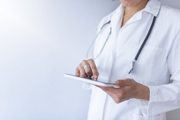 Female doctor holding digital tablet while standing on white background - Foto, imagen