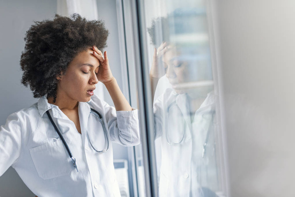 Tired stressed female doctor standing near window - Zdjęcie, obraz