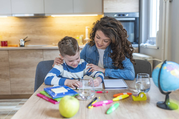 Beautiful businesswoman and cute little son drawing and smiling while sitting in kitchen - Φωτογραφία, εικόνα