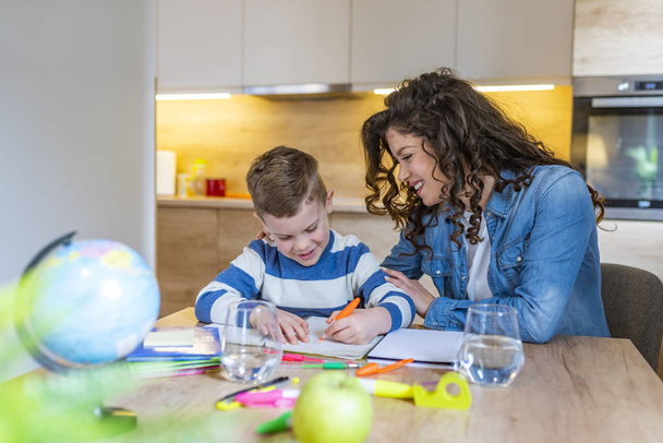 Beautiful businesswoman and cute little son drawing and smiling while sitting in kitchen - Photo, Image