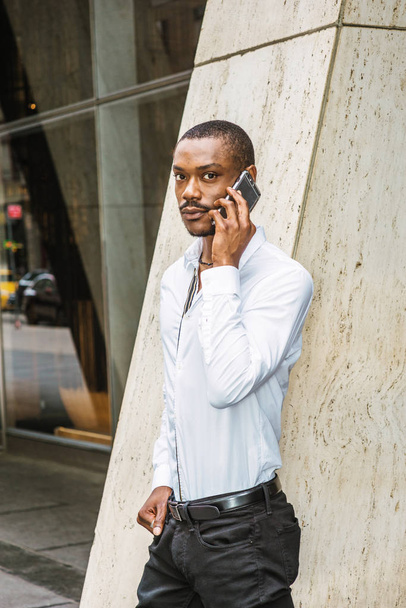 Telefoongesprek buiten. Zakenman van de jonge African American met baard, het dragen van witte shirt, staande op straat buiten kantoor gebouw in New York City, praten op mobiele telefoon - Foto, afbeelding