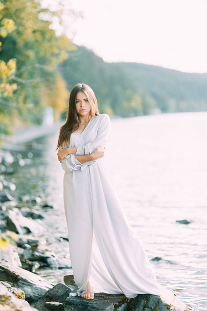 Girl in boudoir dress on the lake, standing and smiling. Unity with nature, morning bride in Russia. Beautiful eyes and model appearance - Foto, Imagem