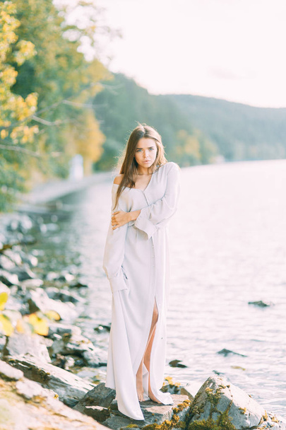 Girl in boudoir dress on the lake, standing and smiling. Unity with nature, morning bride in Russia. Beautiful eyes and model appearance - Фото, зображення