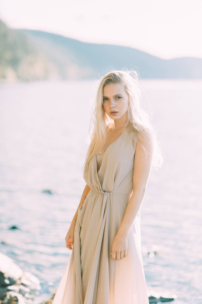 Girl in boudoir dress on the lake, standing and smiling. Unity with nature, morning bride in Russia. Beautiful eyes and model appearance - Foto, Bild