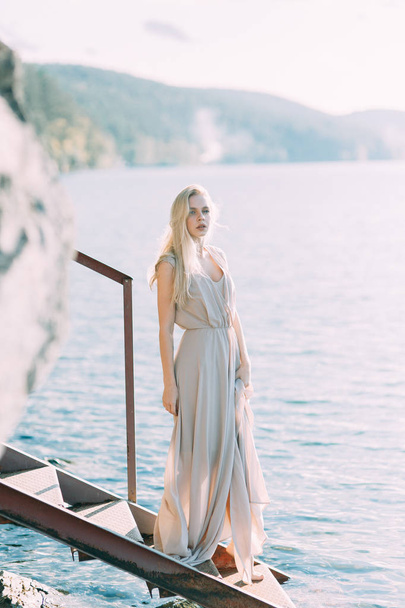 Girl in boudoir dress on the lake, standing and smiling. Unity with nature, morning bride in Russia. Beautiful eyes and model appearance - Foto, imagen