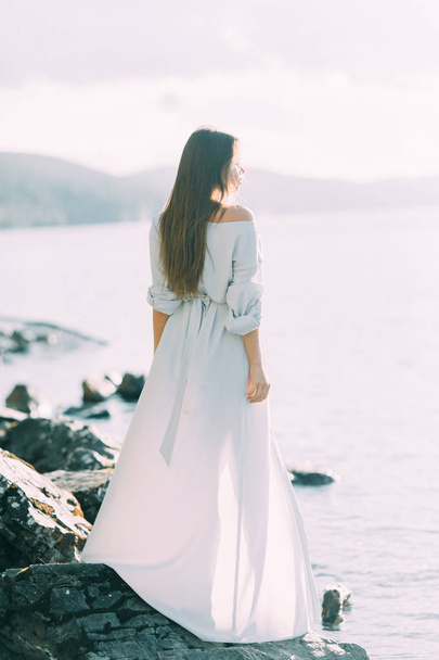 Girl in boudoir dress on the lake, standing and smiling. Unity with nature, morning bride in Russia. Beautiful eyes and model appearance - 写真・画像