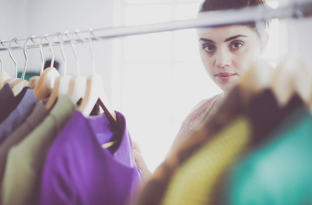 Beautiful young stylist near rack with hangers - 写真・画像