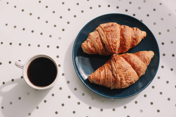 Kávé csésze és friss sült francia croissant kék tányérban, fehér háttérrel. Reggeli. - Fotó, kép