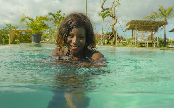 happy and beautiful black afro American woman in bikini having fun at tropical beach resort swimming pool relaxed and playful smiling cheerful enjoying luxury holidays - 写真・画像