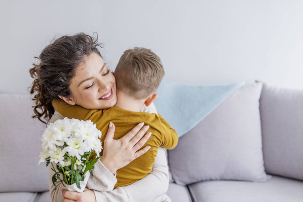 Mother and little son with bouquet of flowers hugging on sofa - Fotoğraf, Görsel