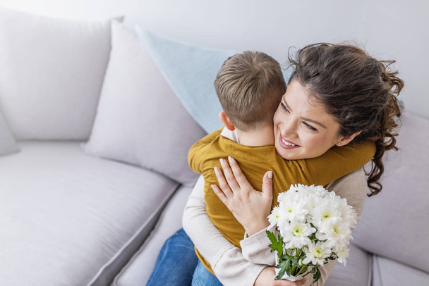 Mother and little son with bouquet of flowers hugging on sofa - Foto, afbeelding