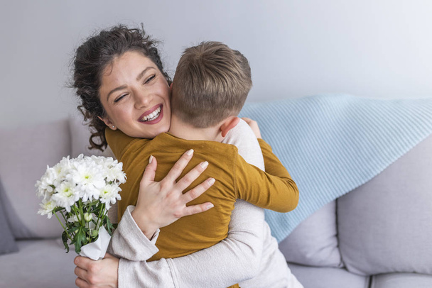 Mother and little son with bouquet of flowers hugging on sofa - Foto, Imagen