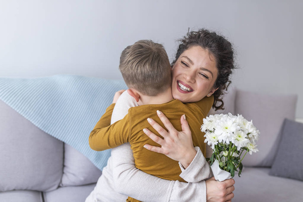 Mother and little son with bouquet of flowers hugging on sofa - Fotografie, Obrázek