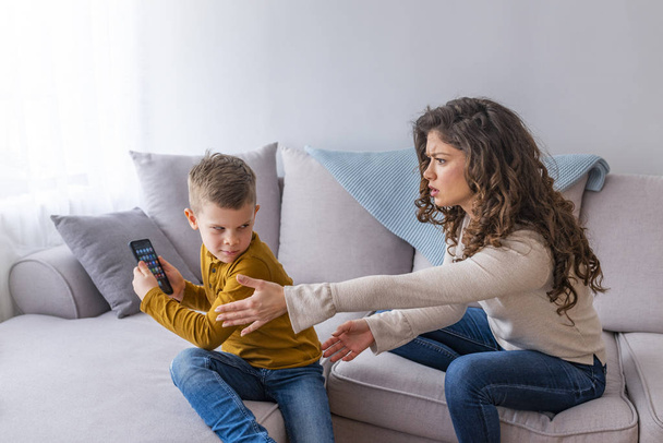Mother scolding child boy playing with phone on couch - Foto, Imagem
