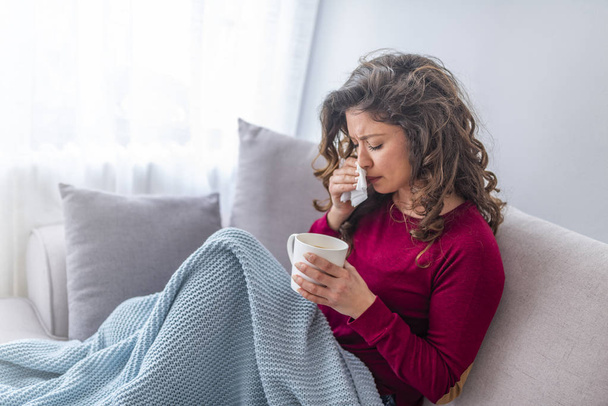 Mladá dívka nemocný v posteli s teplotou kýchání do tkáně a drží horečka pít šálek teplého čaje - Fotografie, Obrázek