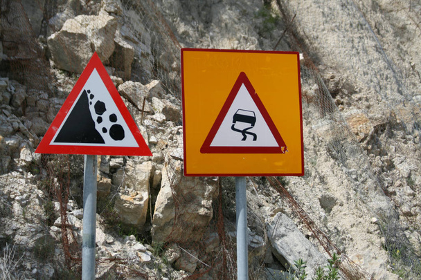 Close-up of a slippery road and a rockfall warning signs in front of a white rocky cliff - Photo, Image
