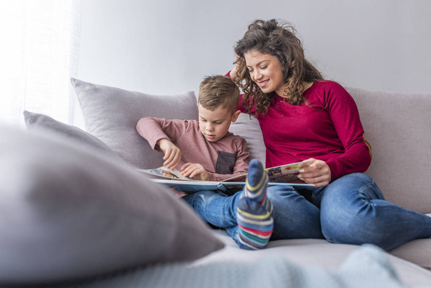 Young woman and little son reading book on sofa - Photo, Image