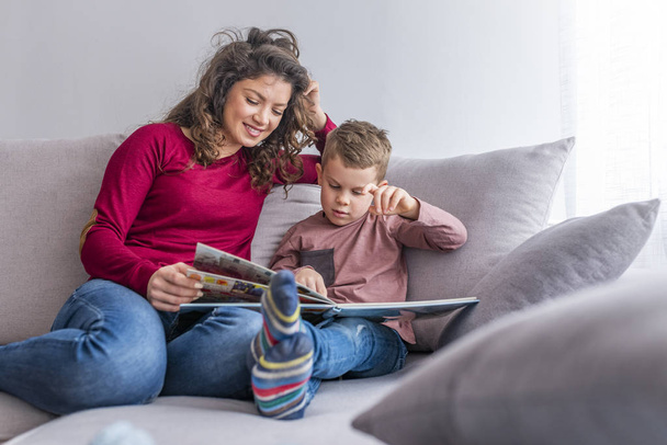 Young woman and little son reading book on sofa - Foto, Imagen