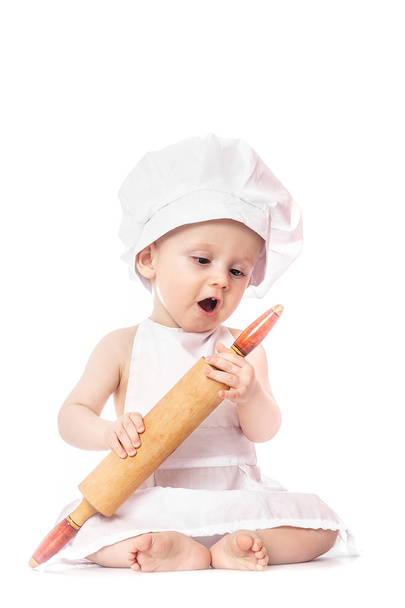 Tien maanden oude baby in een pak van de kok verrast en glimlachend in de keuken. Kleine jongen als een kleine kok of scullion pizza te maken in chef-kok pak. Koken kind levensstijl concept. Peuter spelen. - Foto, afbeelding