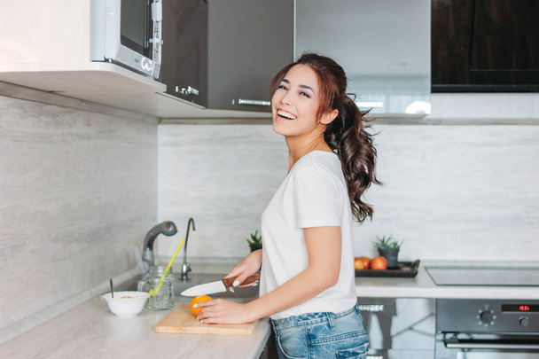 Happy smiling beautiful long hair asian girl young woman cuts lemon in her kitchen - Photo, Image