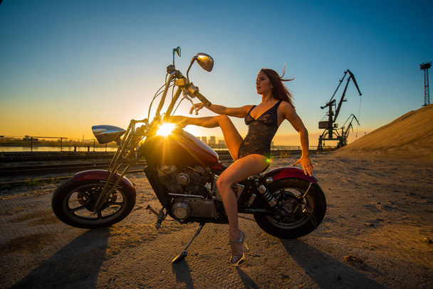 Red-haired woman in sexy lingerie in high heels sits on a motorcycle. Attractive red-haired girl sits on a motorcycle at sunset - Foto, imagen