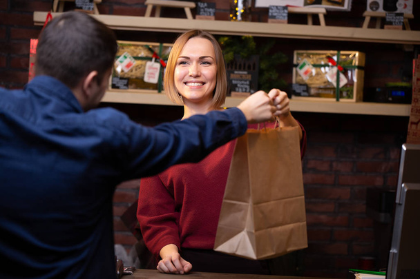 Photo of smiling seller blonde giving paper bag to man - Foto, Bild