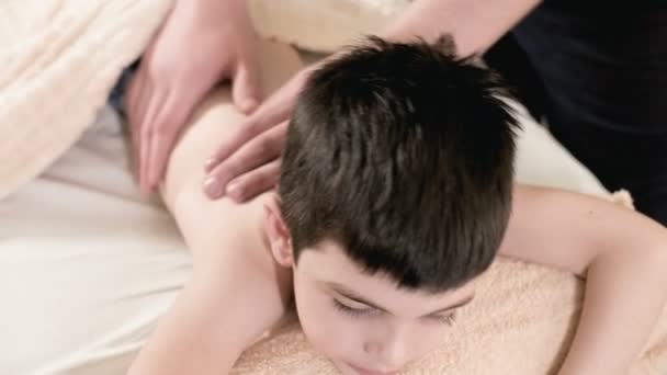 Close-up male physiotherapist masseur makes a healing relaxing massage to a little boy lying on a massage bed. Back massage - Footage, Video