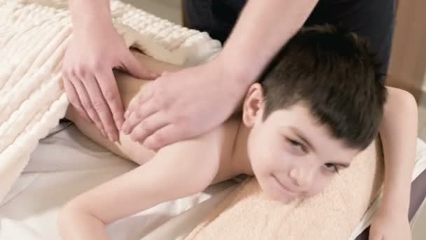 Close-up male physiotherapist masseur makes a healing relaxing massage to a little boy lying on a massage bed. Back massage - Footage, Video