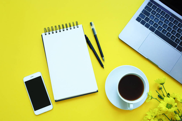 Piso de negocios: escritorio con cuaderno, lápiz, taza de café sobre fondo amarillo
 - Foto, Imagen