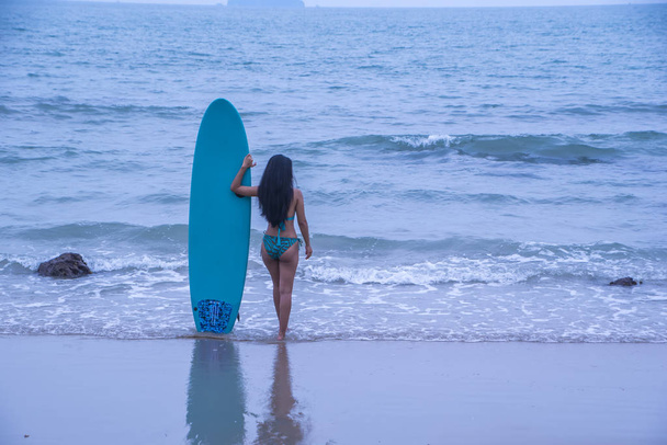 задний вид женщины в бикини с доской для серфинга перед океаном
 - Фото, изображение