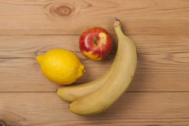 木製の背景にバナナとレモン リンゴ。上からの眺め . - 写真・画像