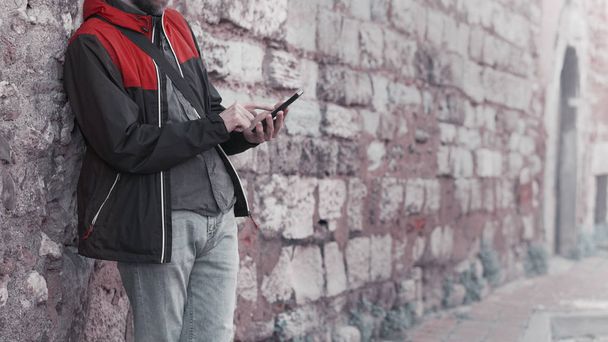 Young man standing against a wall background and using smartphone. Technology and lifestyle concept.                                - 写真・画像