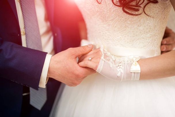 Close-up of hands of romantic couple holding together during wedding ceremony. Elegant groom holds bride's hand with wedding ring. - Фото, зображення