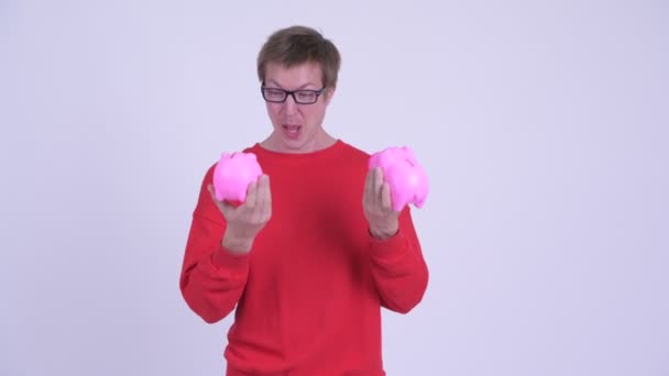 Happy young man playing with two piggy banks - Footage, Video