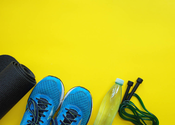 Fitness background. Equipment for gym and home. Jump rope,  mat, water, sneakers  on yellow background top view copy space - Photo, Image