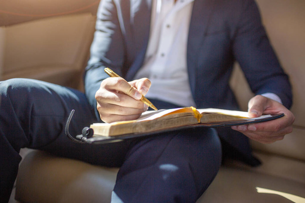 Cut view of mans body in suit sitting in luxury car and making notes in notebook. - Foto, imagen