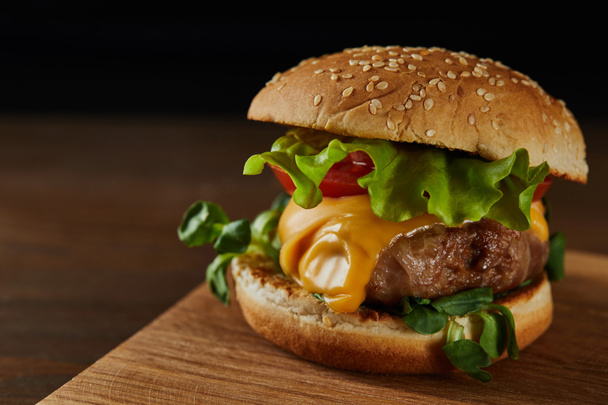 close up of tasty meat burger with cheese and greenery on wooden chopping board - Фото, зображення