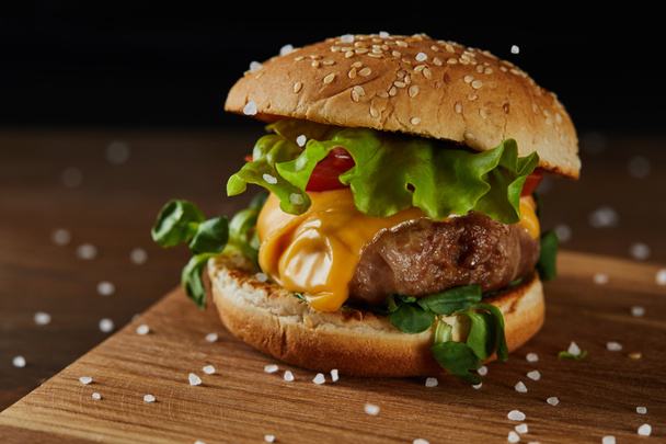 close up of tasty meat burger with salt on wooden chopping board - Foto, Imagem