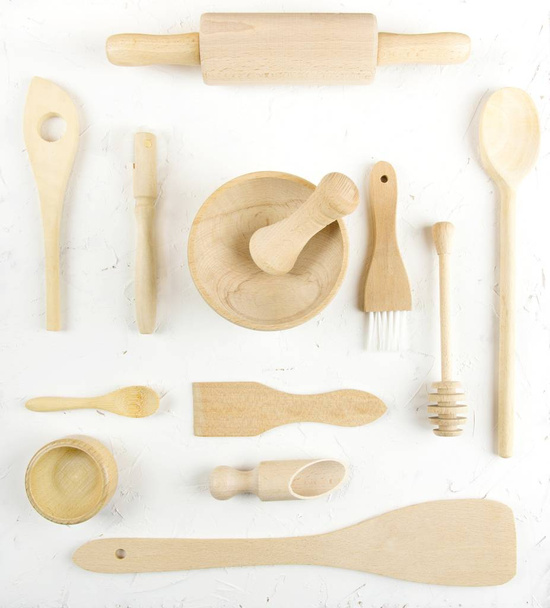 A flat lay overhead view of various wooden kitchen utensils on a white structured background - Foto, imagen