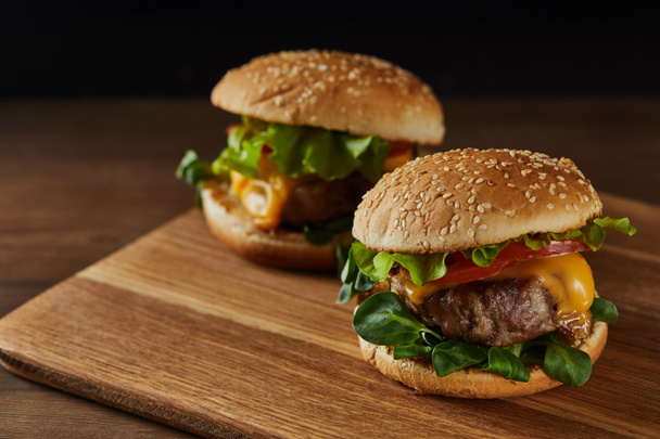 tasty meat burgers with melted cheese on wooden chopping board - Fotografie, Obrázek