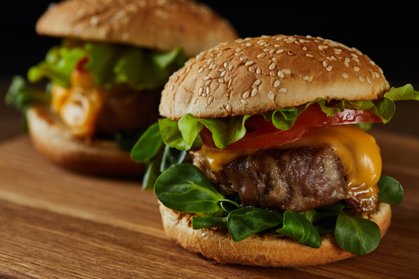 selective focus of tasty meat burgers with cheese and greenery on wooden chopping board - Fotoğraf, Görsel