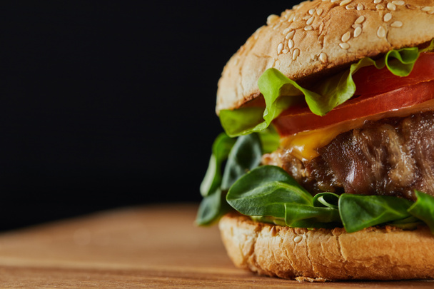 close up of delicious meat burger with cheese, greenery and sesame isolated on black - Photo, Image