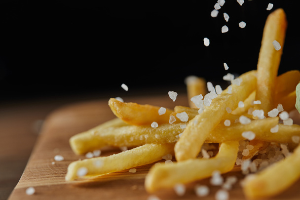 close up of salt falling on fresh golden french fries on wooden chopping board - Photo, Image