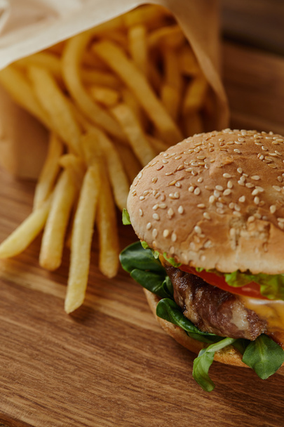 selective focus of delicious burger with sesame on bun and french fries on wooden surface - Fotografie, Obrázek