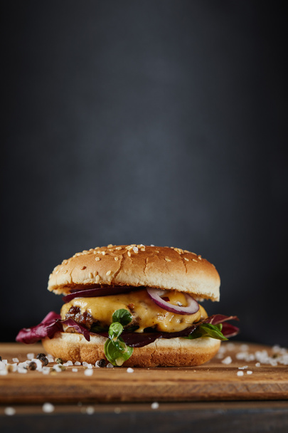seasoning and delicious burger with meat, cheese and onions on dark background - Foto, Bild