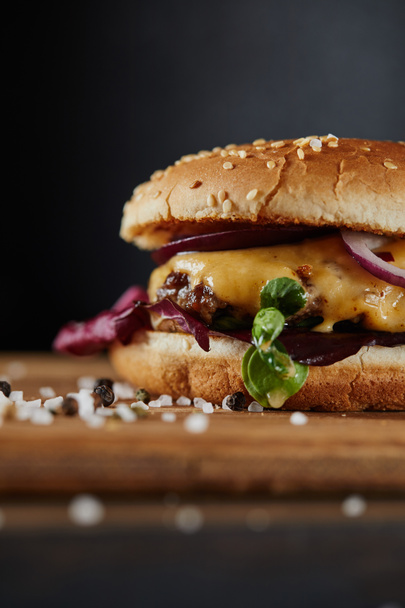 selective focus of seasoning and delicious burger with meat, cheese and onions on dark background - Photo, Image