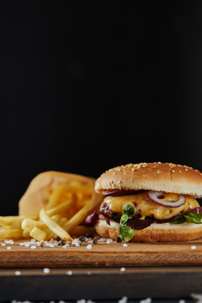 selective focus of salt, french fries and delicious burger with meat on wooden surface isolated on black - Zdjęcie, obraz