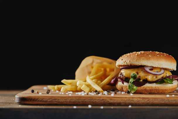 salt and pepper, french fries and delicious burger with meat on wooden surface isolated on black - Zdjęcie, obraz