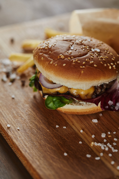salt, pepper, french fries and fresh delicious burger on wooden surface  - Foto, Imagen