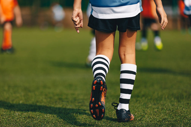 Nohy kluk fotbalista ve Fotbalové kopačky boty. Hráč na zelené travnaté fotbalové hřiště na stadionu. Detail z fotbalové sportovní vybavení  - Fotografie, Obrázek